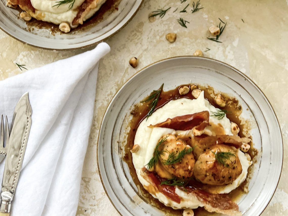 Photograph of Seared Scallops and Creamed Cauliflower with Hazelnut, Soy, Lime and Chilli Dressing, topped with Cured Meat Chips and Roast Hazelnuts.