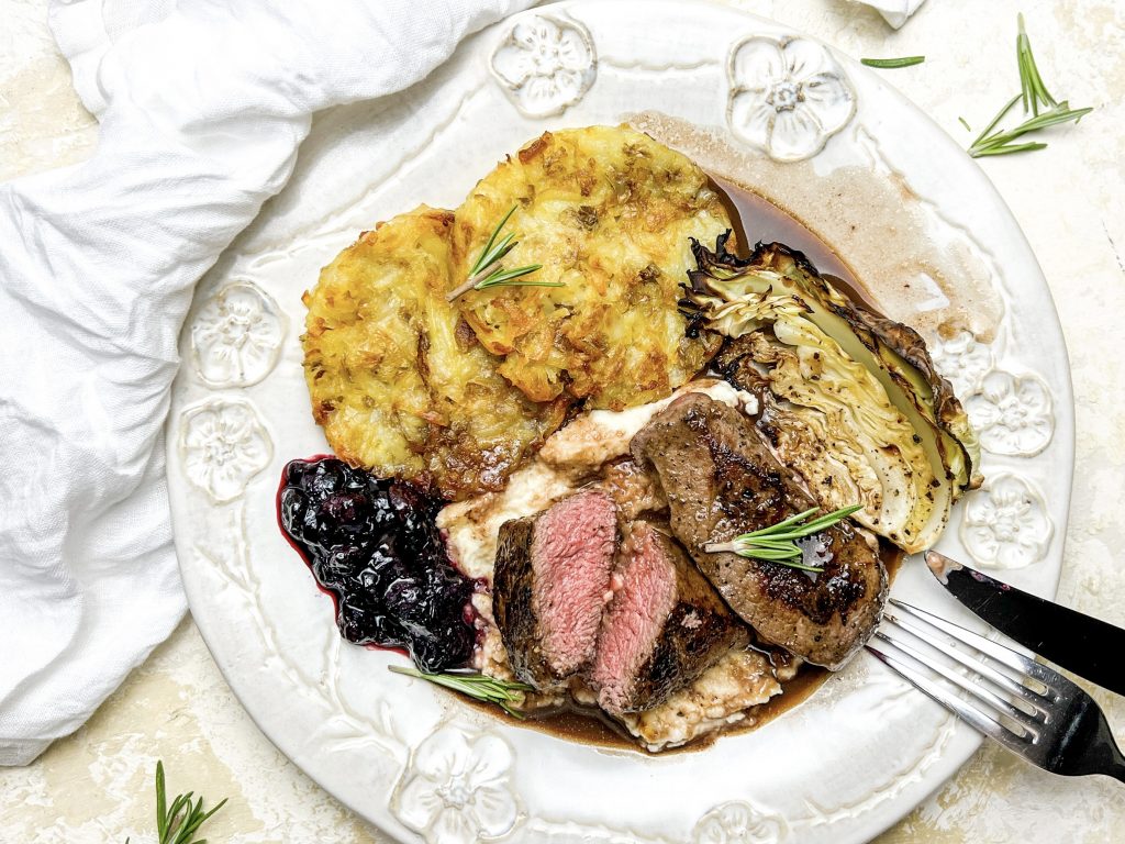 Photograph of Pan-fried Venison Fillet, Potato Cakes, Celeriac Purée, Roast Cabbage, Red Wine Jus and Macerated Blueberries